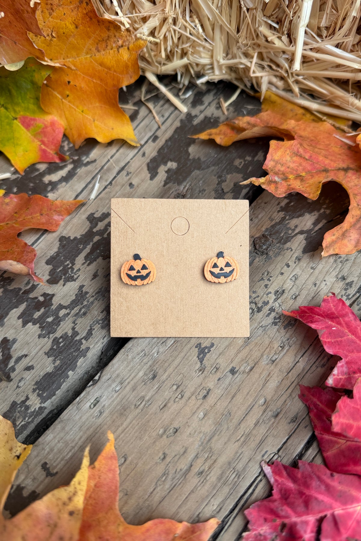 Jack-o-lantern Halloween stud earrings styled with fall leaves
