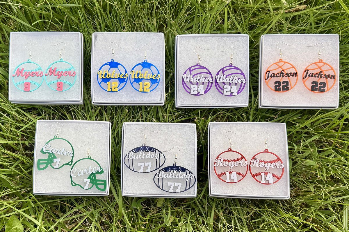 Collection of personalized sports earrings featuring softball, soccer, volleyball, basketball, football helmet, football, and baseball designs customized with player names, numbers, and team colors.