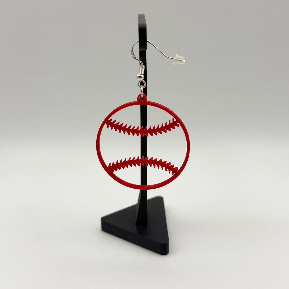 Red baseball earring with open stitching design displayed on a black stand.