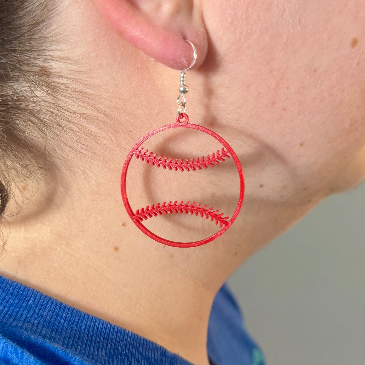 Red baseball earring with open stitching design being worn.