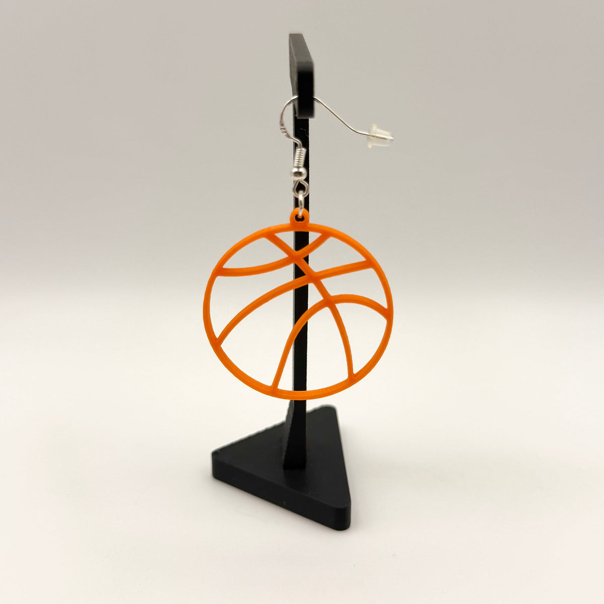 Orange basketball earring with open line design displayed on a black stand.