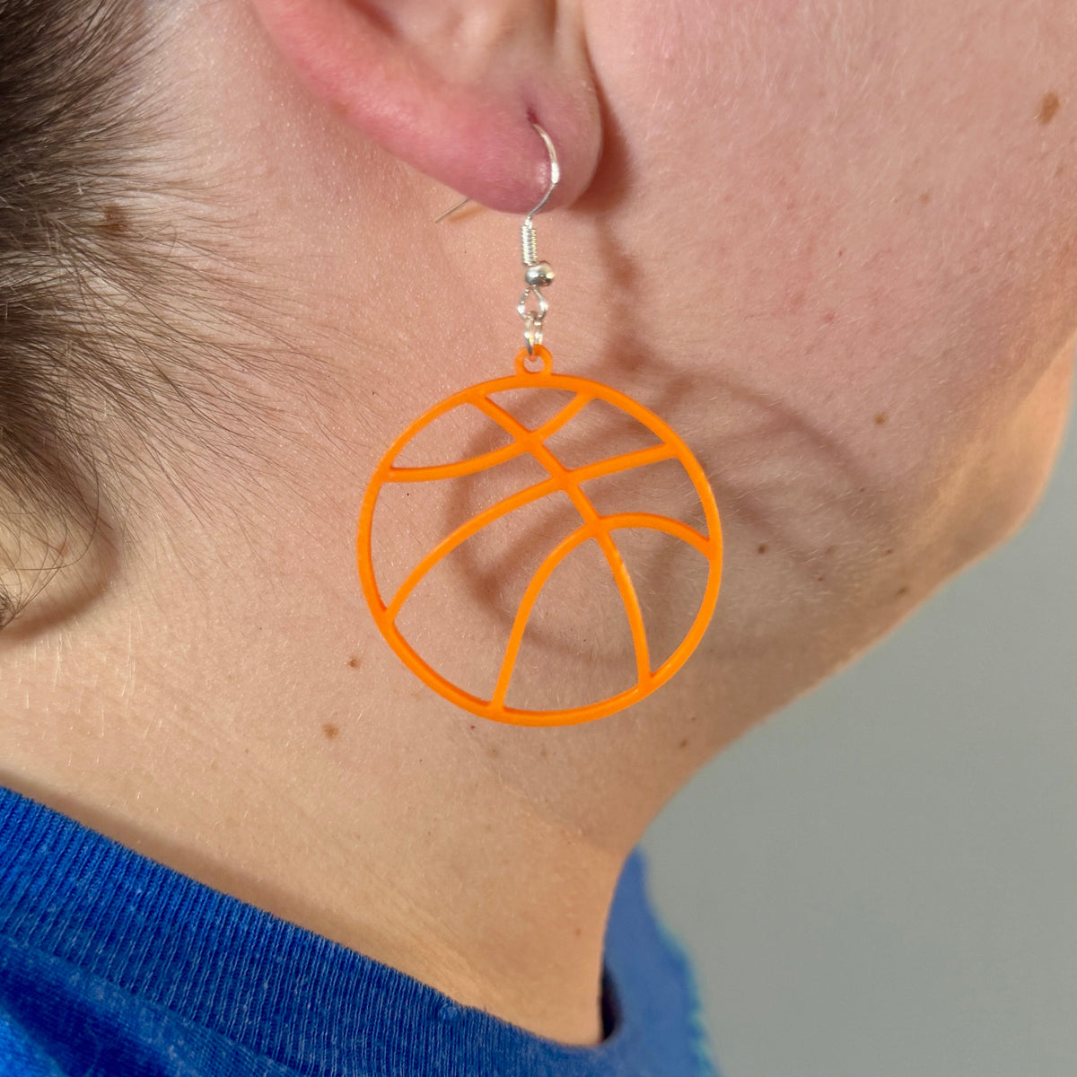 Orange basketball earring with open line design being worn.