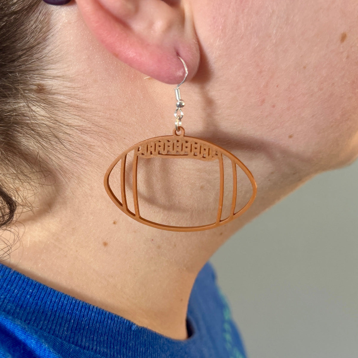 Brown football earring with open line design being worn.
