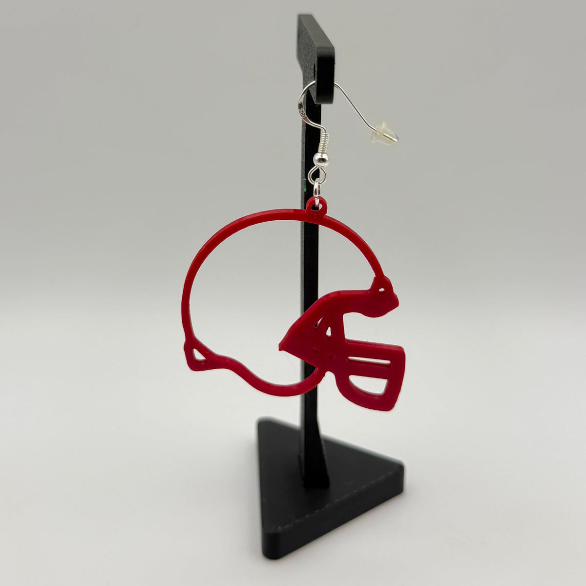 Red football helmet earring with open design displayed on a black stand.
