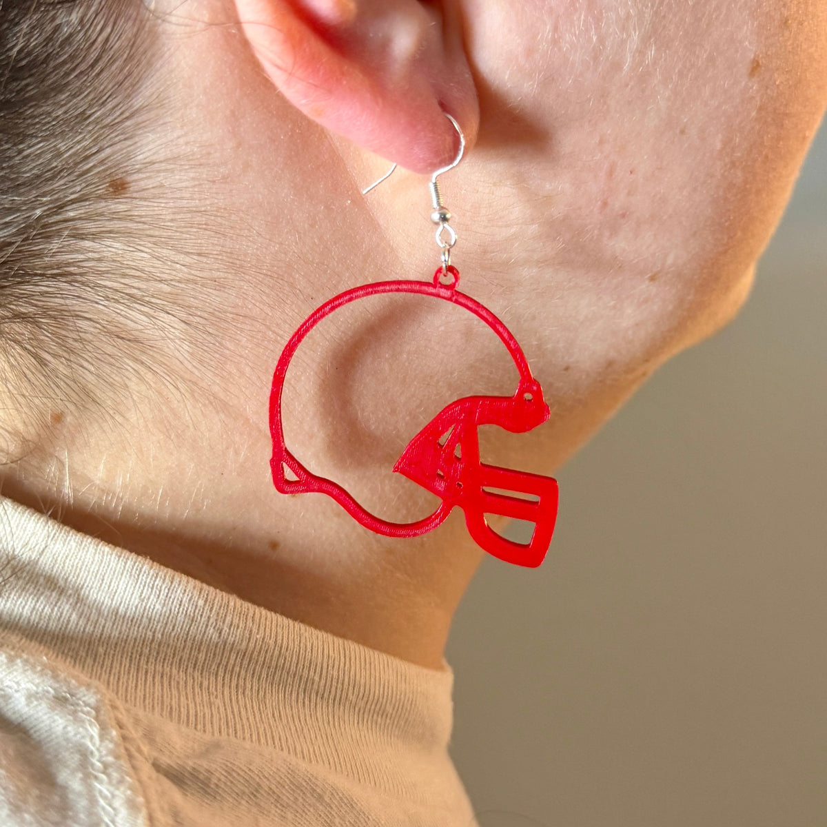 Red football helmet earring with open design being worn.