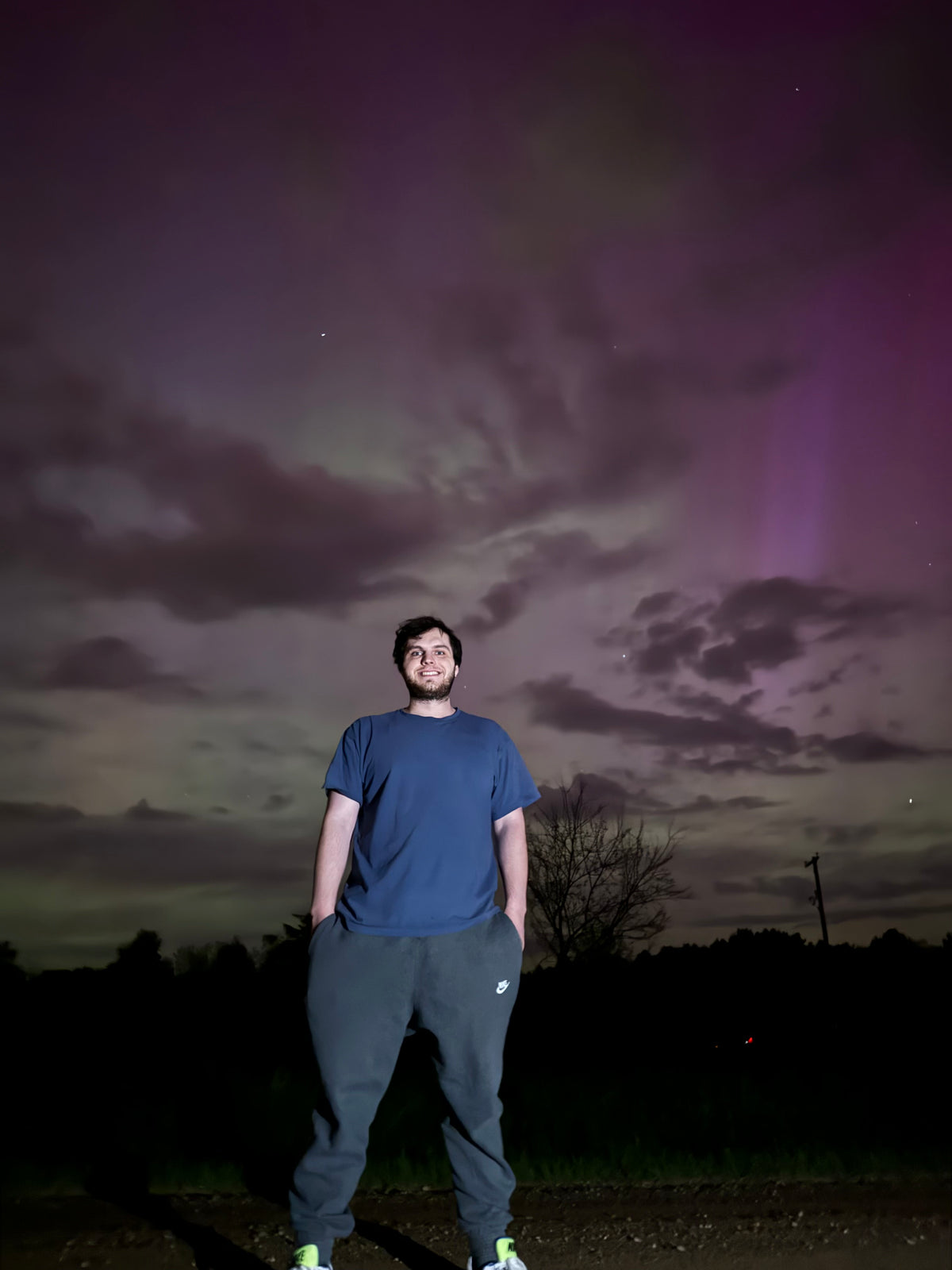 Man standing outdoors at night beneath a purple and green aurora-filled sky.