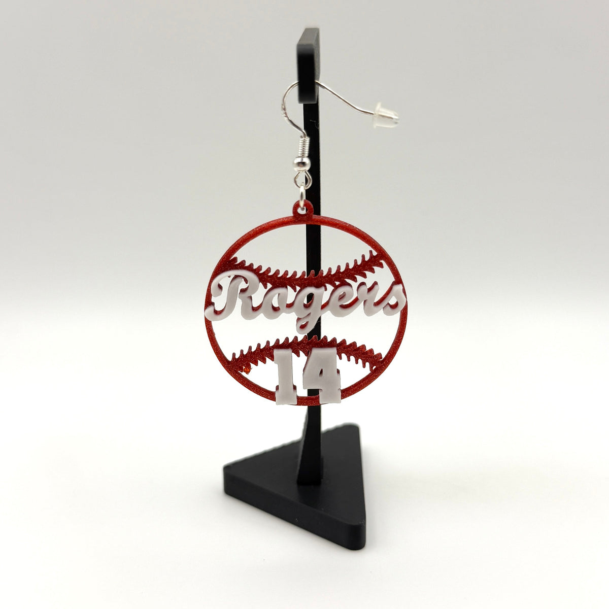 Red and white personalized baseball earring with Rogers and number 14 displayed on a black stand.