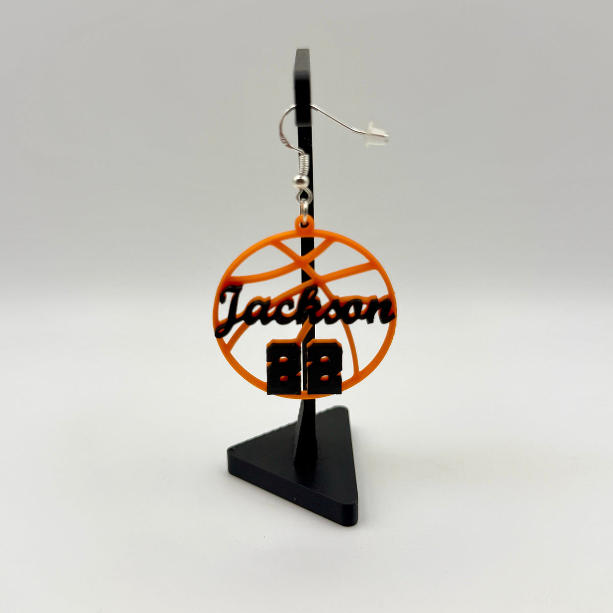 Orange and black personalized basketball earring with Jackson and number 22 displayed on a black stand.