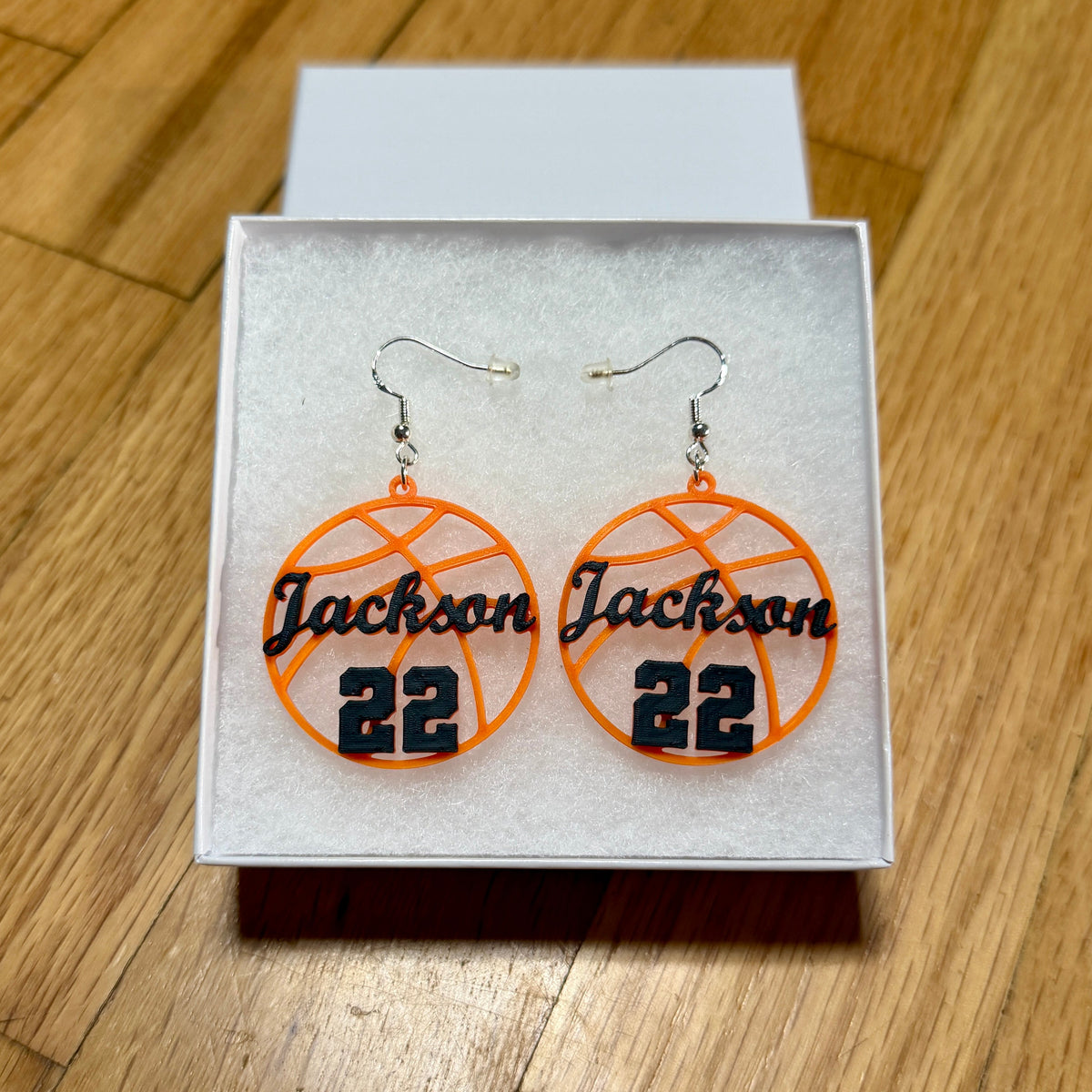Pair of orange and black personalized basketball earrings with Jackson and number 22 displayed in a jewelry box.