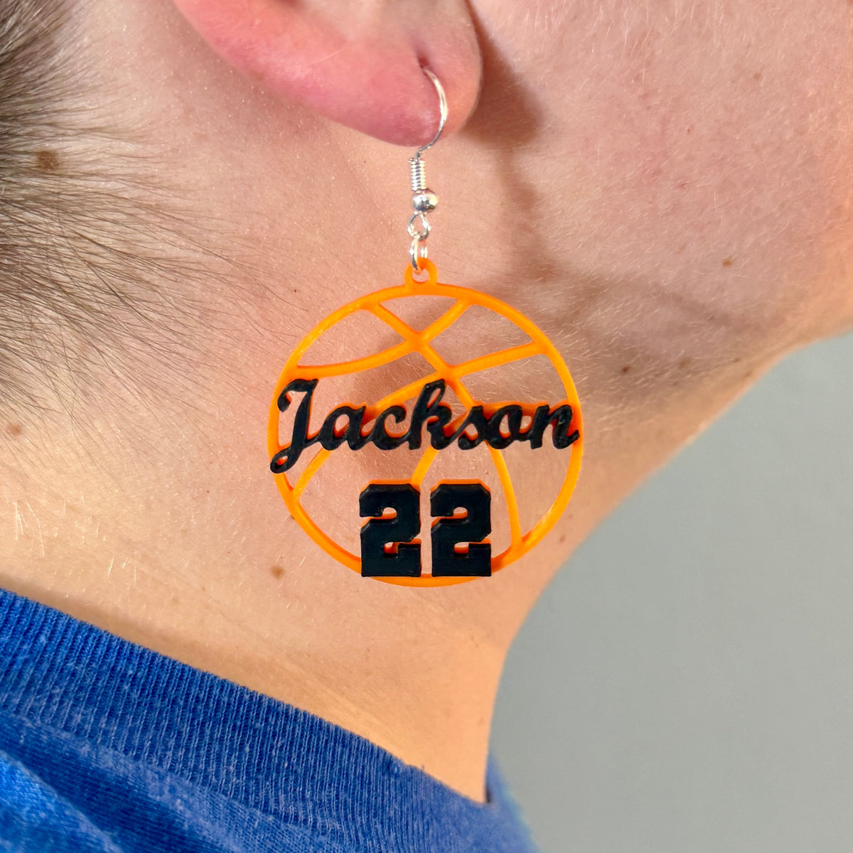 Personalized orange and black basketball earring with Jackson and number 22 being worn.