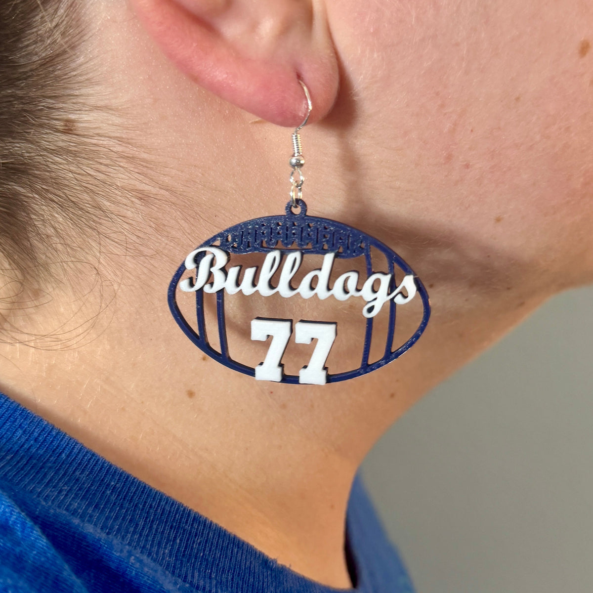 Personalized blue and white football earring with Bulldogs and number 77 being worn.