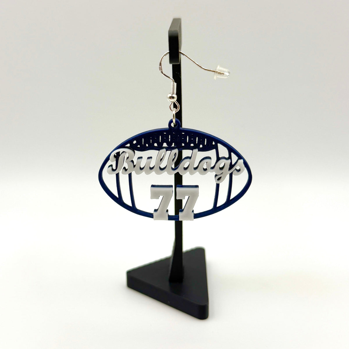 Blue and white personalized football earring with Bulldogs and number 77 displayed on a black stand.