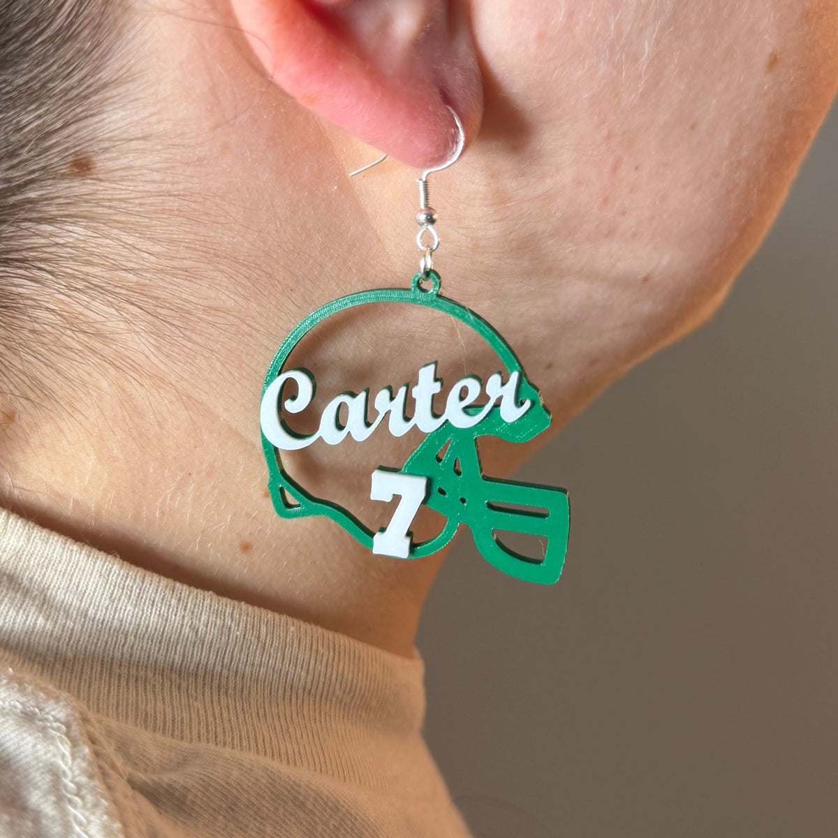 Personalized green and white football helmet earring with Carter and number 7 being worn.