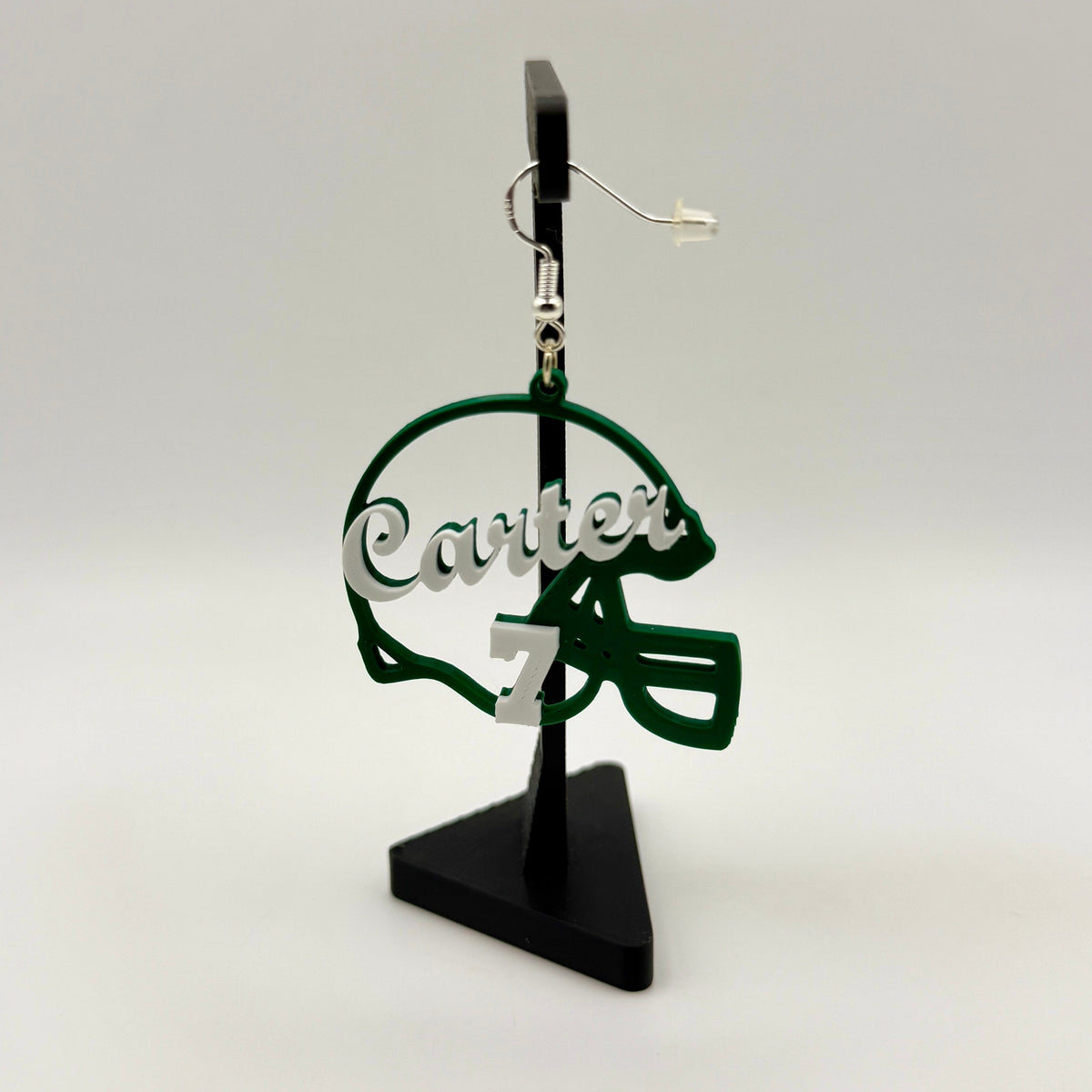 Green and white personalized football helmet earring with Carter and number 7 displayed on a black stand.