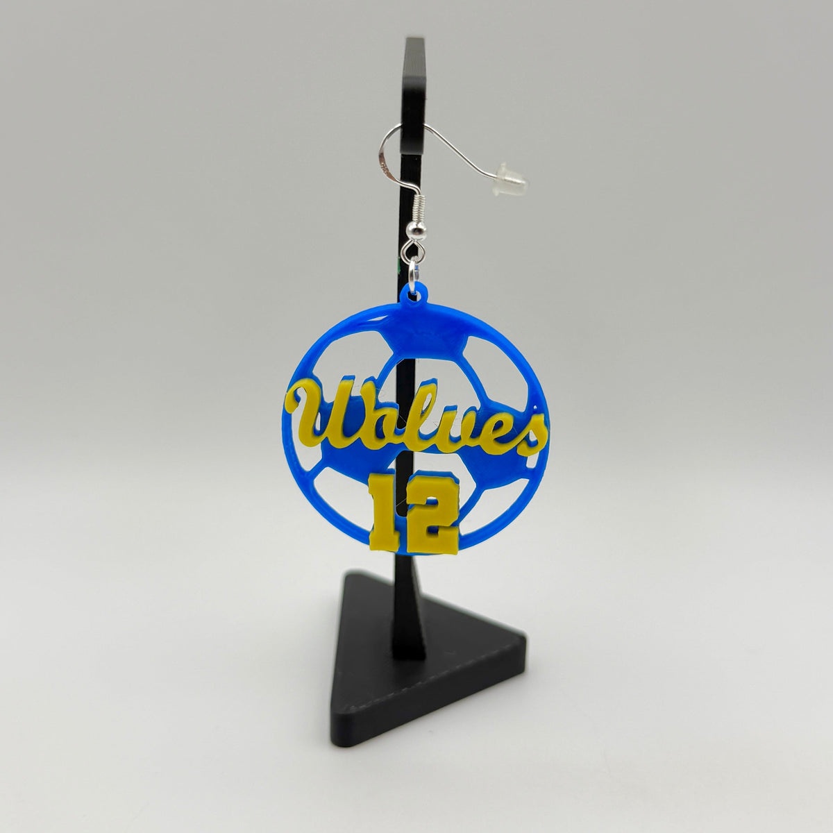 Blue and yellow personalized soccer earring with Wolves and number 12 displayed on a black stand.