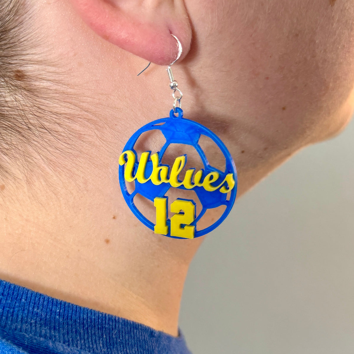 Personalized blue and yellow soccer earring with Wolves and number 12 being worn.