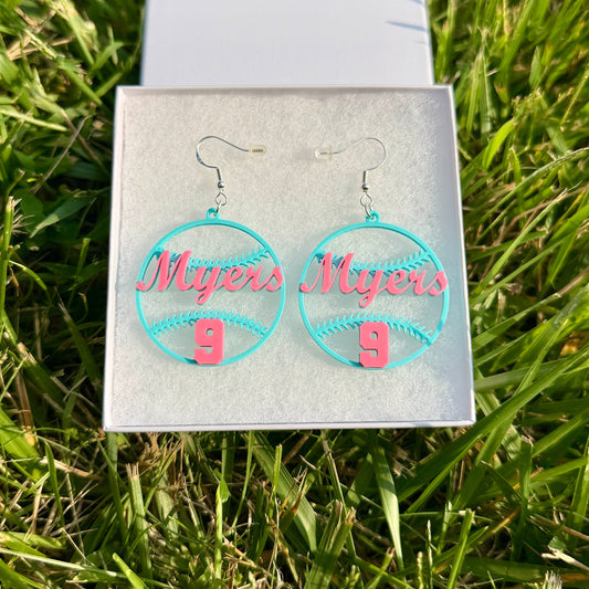 Pair of teal and pink personalized softball earrings with Myers and number 9 displayed in a jewelry box on grass.