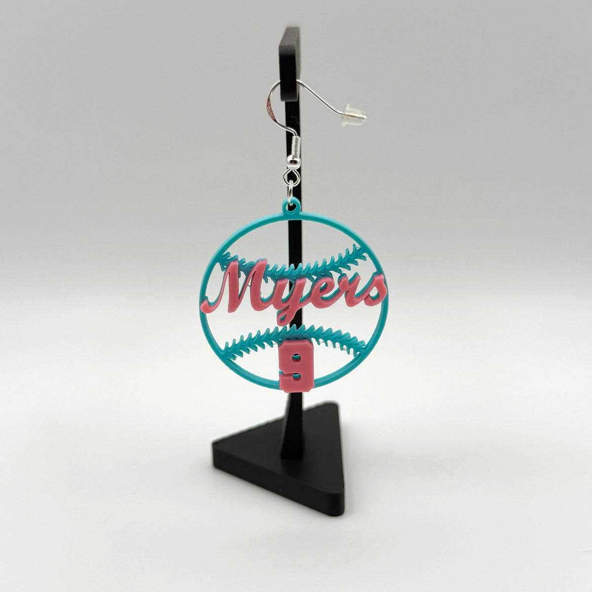Teal and pink personalized softball earring with Myers and number 9 displayed on a black stand.