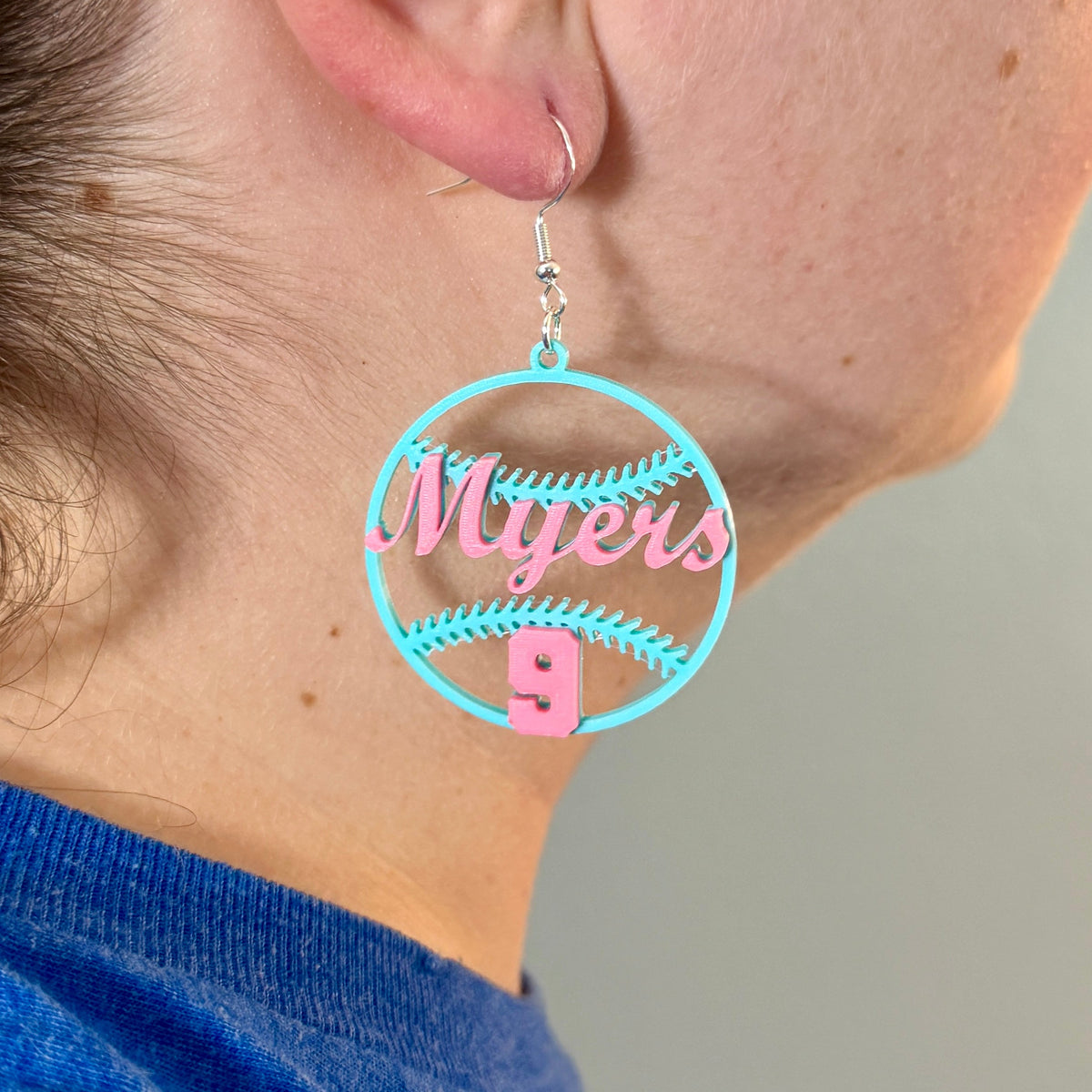 Personalized teal and pink softball earring with Myers and number 9 being worn.