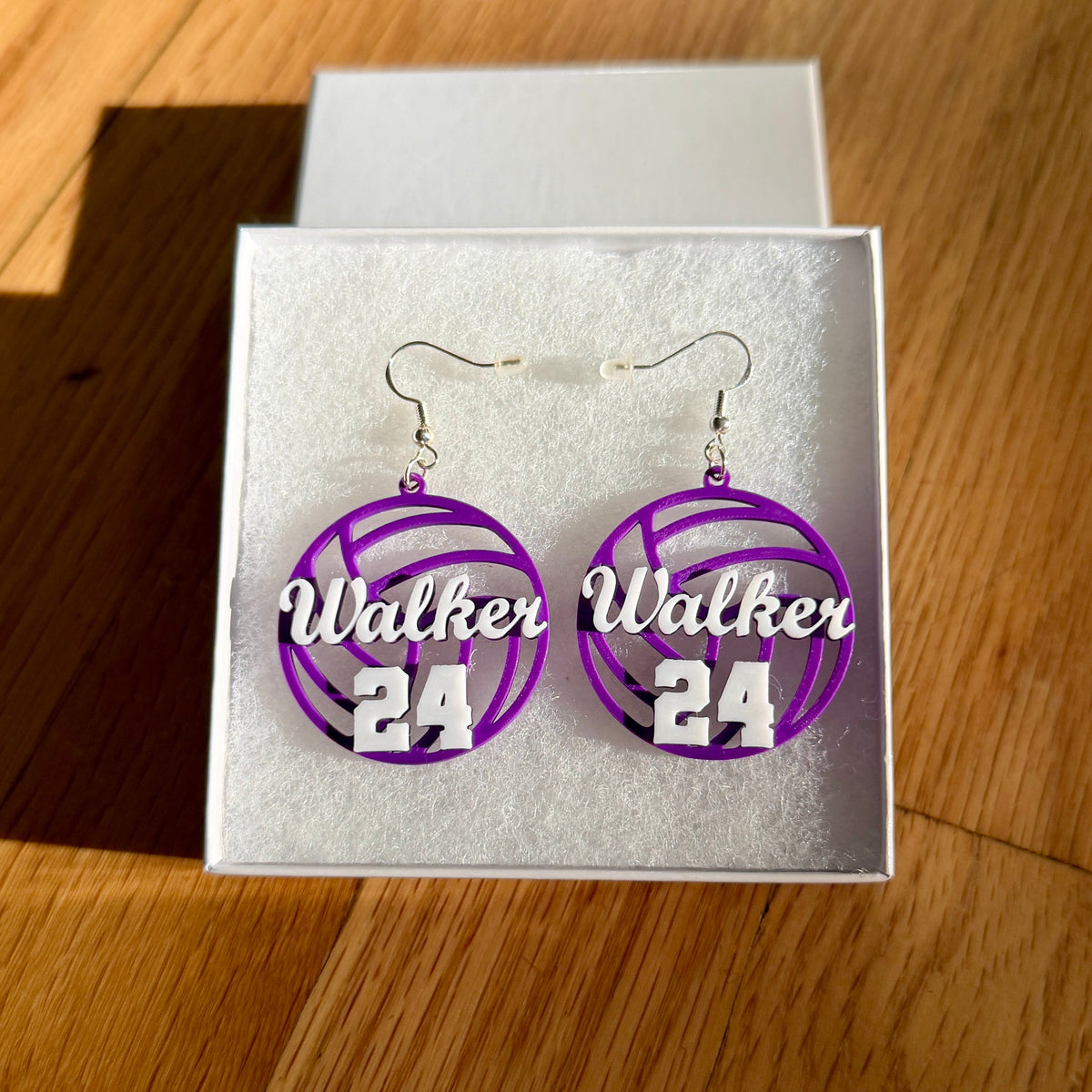 Pair of purple and white personalized volleyball earrings with Walker and number 24 displayed in a jewelry box.