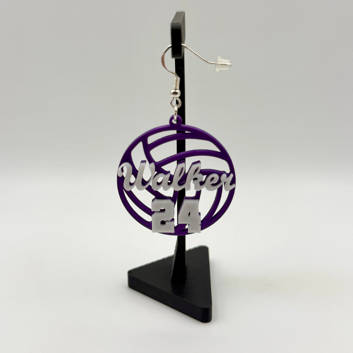 Purple and white personalized volleyball earring with Walker and number 24 displayed on a black stand.