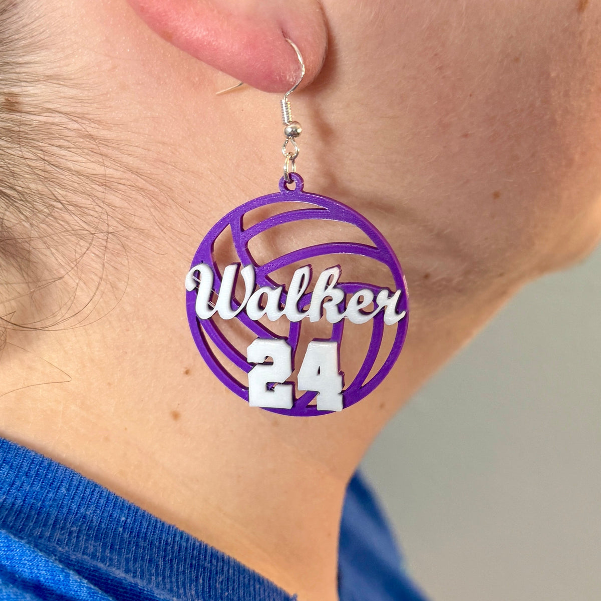 Personalized purple and white volleyball earring with Walker and number 24 being worn.