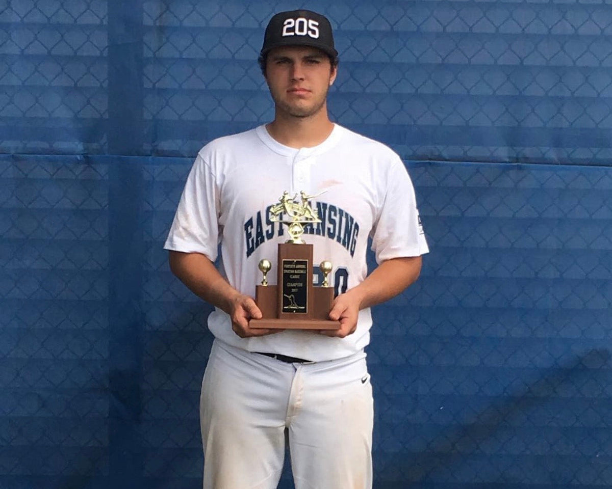 Young baseball player in uniform holding a championship trophy in front of a blue dugout fence.