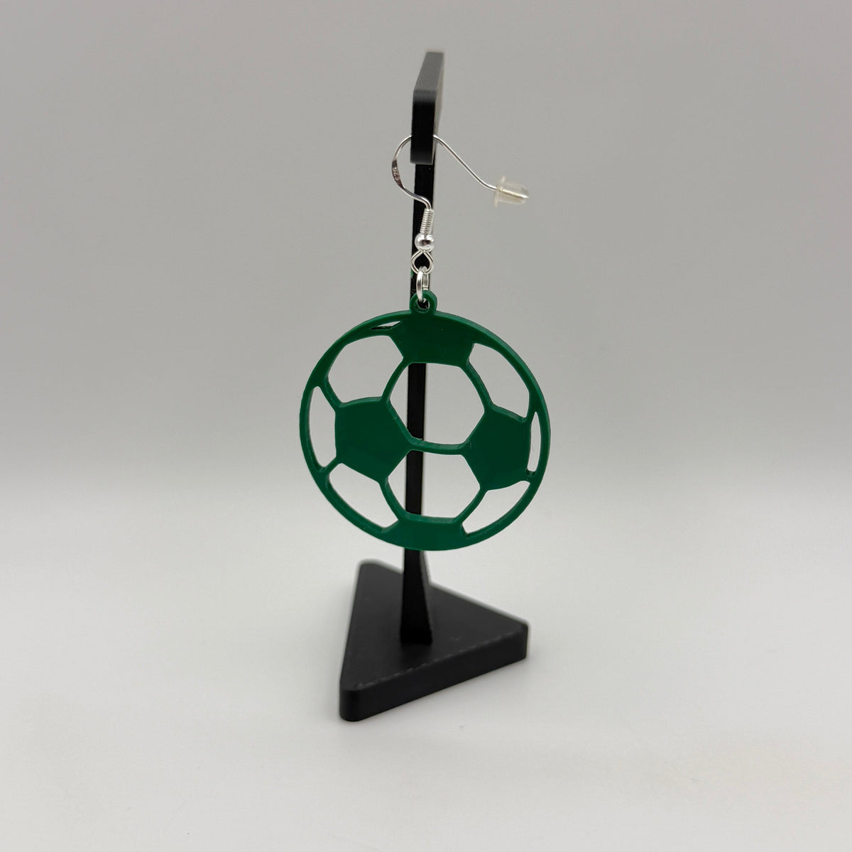 Green soccer ball earring with open panel design displayed on a black stand.