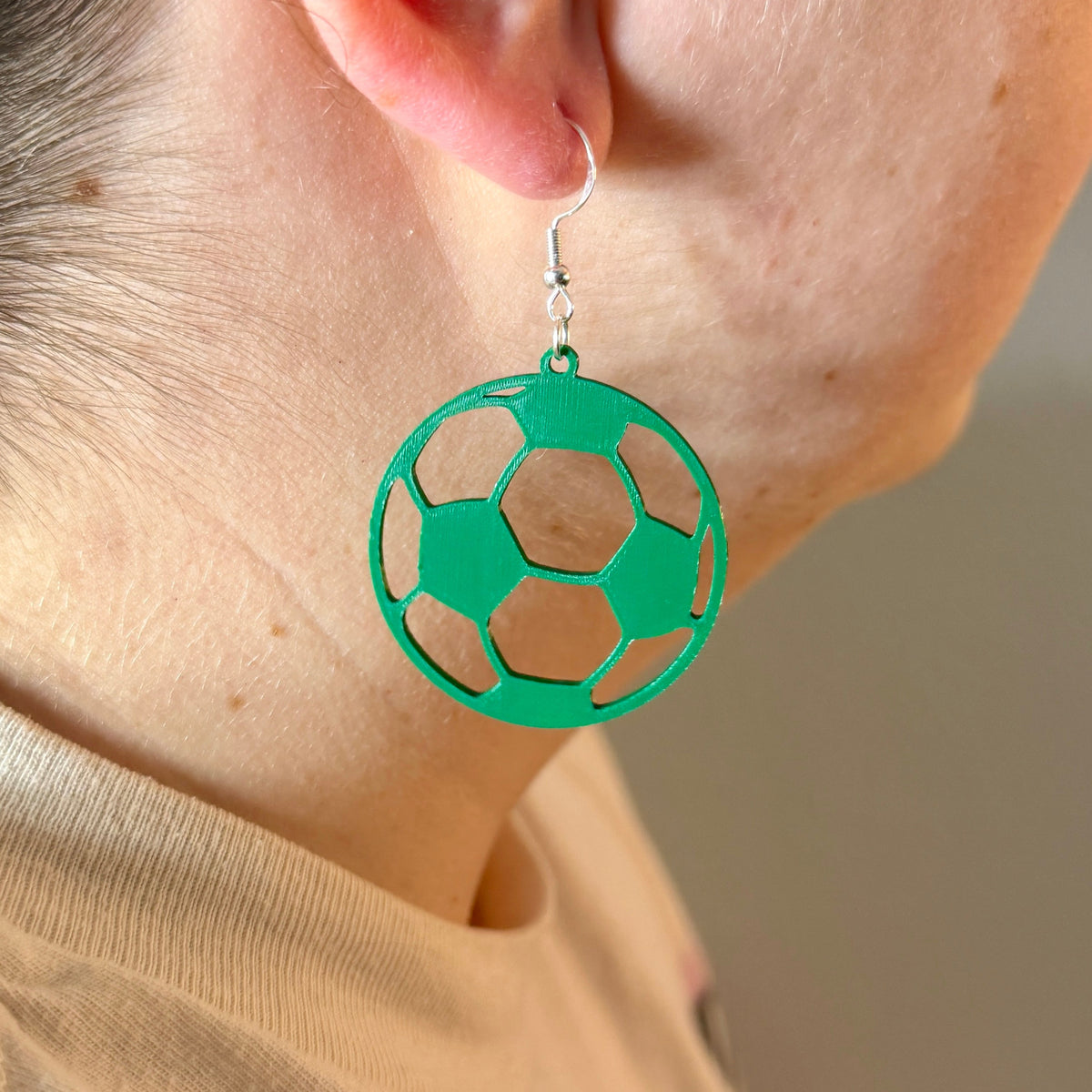 Green soccer ball earring with open panel design being worn.
