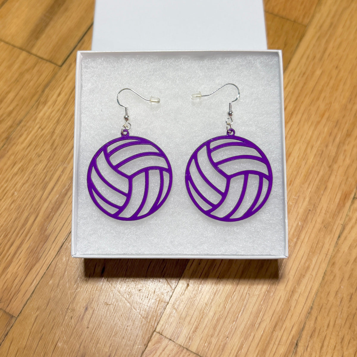 Pair of purple volleyball earrings with open panel design displayed in a jewelry box.