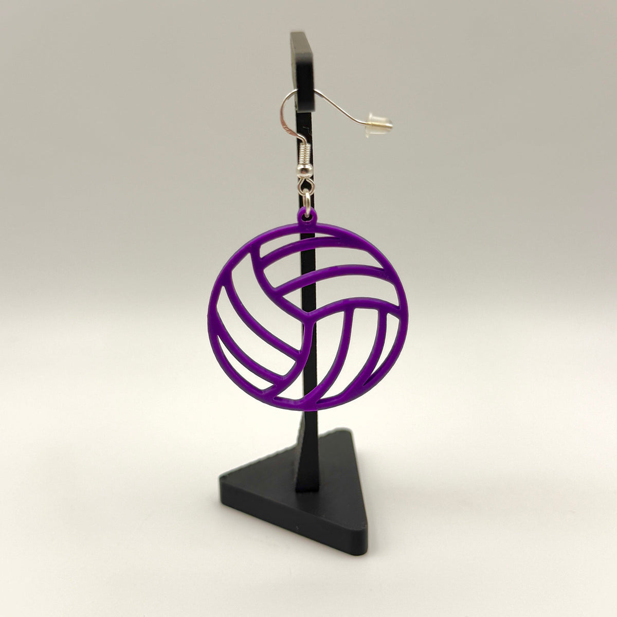 Purple volleyball earring with open panel design displayed on a black stand.