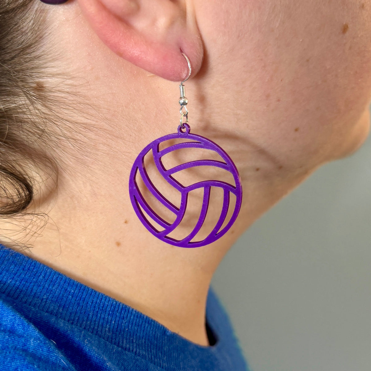 Purple volleyball earring with open panel design being worn.